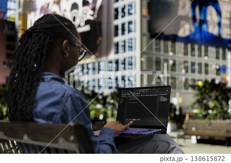 Software developer on park bench writes code on laptop, implementing algorithms. Female programmer using programming languages script program on notebook display, freelancing outdoors 138615872