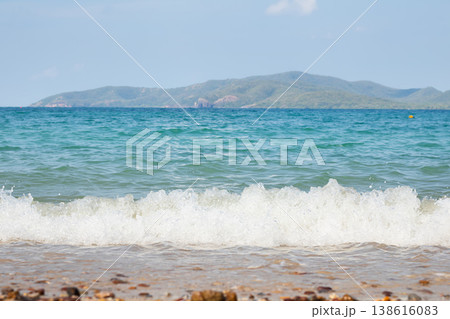 Vivid turquoise sea wave splashes onto a sandy pebble beach, with a lush island stretching across the horizon under a bright blue sky, capturing a refreshing tropical coastal atmosphere. Vivid turquoise sea wave splashes onto a sandy pebble beach, with a lush island stretching across the horizon under a bright blue sky, capturing a refreshing tropical coastal atmosphere. 138616083