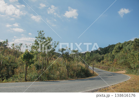 Winding asphalt road through green countryside hills under blue sky, scenic rural landscape with travel and journey concept. 138616176