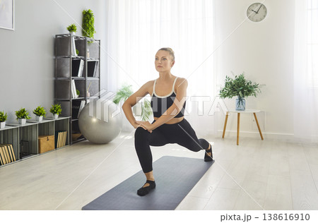 Sporty fit woman performing lunge stretch on mat, stretching body, engaging in exercise Sporty fit woman performing lunge stretch on mat, stretching body, engaging in exercise 138616910
