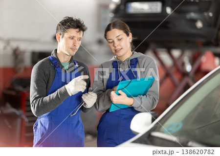 Car service manager discusses car repair problems with mechanic. He takes notes on paper 138620782