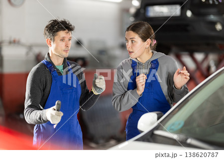 Two auto mechanics, man and woman, diagnosing a car engine together in car repair shop Two auto mechanics, man and woman, diagnosing a car engine together in car repair shop 138620787
