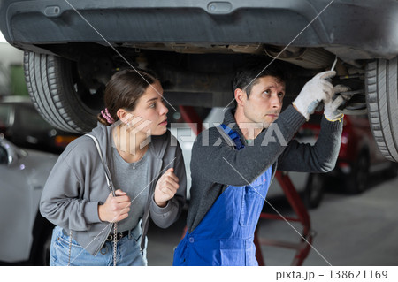 Girl watches as a professional mechanic repairs her car at car service center Girl watches as a professional mechanic repairs her car at car service center 138621169