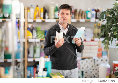 Man buyer chooses shampoo or shower gel in household goods department of supermarket Man buyer chooses shampoo or shower gel in household goods department of supermarket 138621199