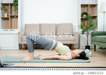 Asian woman practicing yoga and home workout in a bright living space. Healthy lifestyle, fitness, balance, and mindfulness concept with calm and modern atmosphere. 138621212
