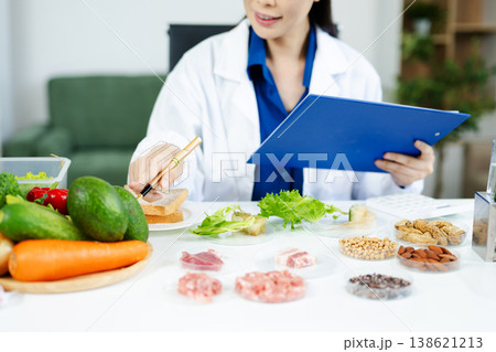 Nutritionist woman in lab coat analyzing vegetables, meat, grains in a modern food science lab. Healthy lifestyle, diet research, clinical testing Nutritionist woman in lab coat analyzing vegetables, meat, grains in a modern food science lab. Healthy lifestyle, diet research, clinical testing 138621213