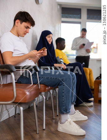 Guy teenager waiting in line at reception with phone in his hand Guy teenager waiting in line at reception with phone in his hand 138621285
