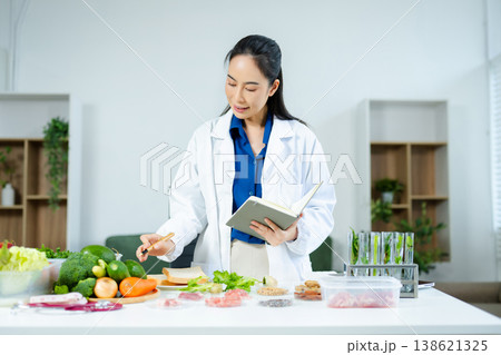 Female nutritionist in lab coat analyzing food and writing in notebook. Healthy eating, organic testing, and nutrition science in a clean lab. Female nutritionist in lab coat analyzing food and writing in notebook. Healthy eating, organic testing, and nutrition science in a clean lab. 138621325