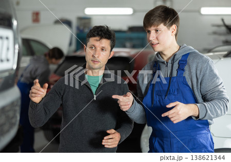 Adult car owner discusses with a young auto mechanic the cost and time of car repairs at car service center Adult car owner discusses with a young auto mechanic the cost and time of car repairs at car service center 138621344