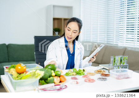 Professional nutritionist reviewing fresh vegetables and supplements for diet planning, health care, and wellness in a clinical nutrition setting 138621364