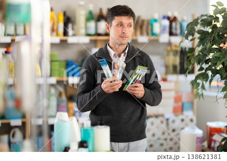 Among shop windows, man buyer leisurely examines goods and chooses toothbrush 138621381