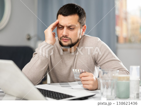 Man with pills in his hands is looking for diagnosis on the Internet using laptop Man with pills in his hands is looking for diagnosis on the Internet using laptop 138621436
