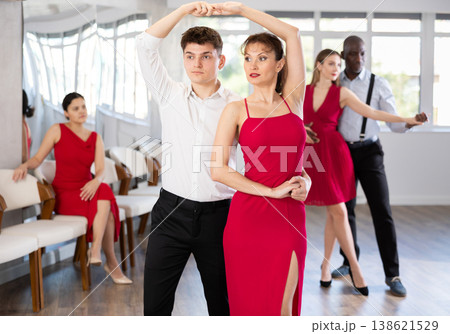 Happy young woman dressed in red dress with man in elegant clothes dancing bachata in ballroom dance class Happy young woman dressed in red dress with man in elegant clothes dancing bachata in ballroom dance class 138621529