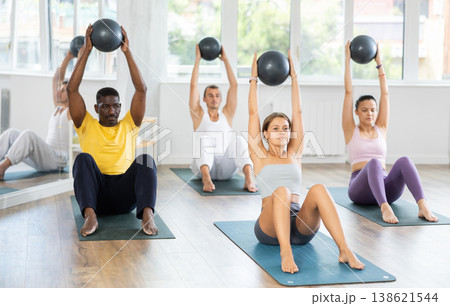 Pilates class in multi-ethnic group - men and women hold the ball above their heads and do bends 138621544