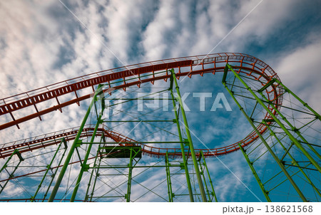 Intricate green steel support beams and orange tracks viewed from below against a cloudy sky 138621568