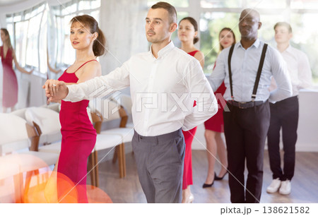 Confident man dancing waltz with female partner in red during group class 138621582