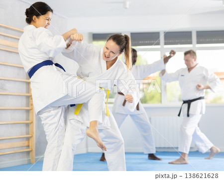 Middle-aged woman attendee of karate classes fighting with her opponent in sports hall Middle-aged woman attendee of karate classes fighting with her opponent in sports hall 138621628