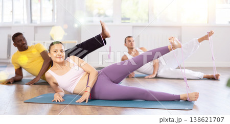 Pilates class - group of people of different nationalities doing leg stretches using resistance bands in gym Pilates class - group of people of different nationalities doing leg stretches using resistance bands in gym 138621707