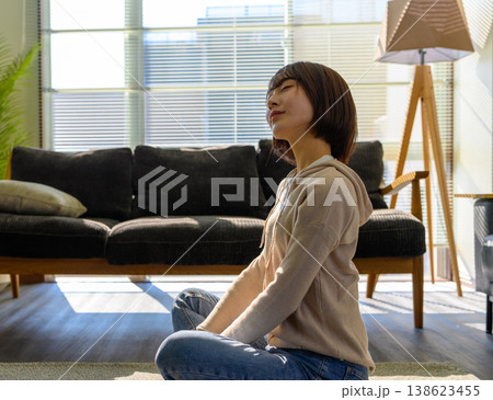 女性がリビングで瞑想する 女性がリビングで瞑想する 138623455