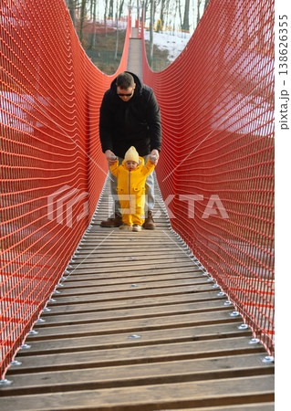 Father holding toddler on red suspension bridge in winter forest 138626355