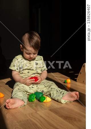 Toddler playing with toy vegetables on sunlit wooden floor 138626407