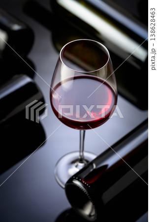 Glass and bottles of red wine on a black reflective background. Glass and bottles of red wine on a black reflective background. 138628463