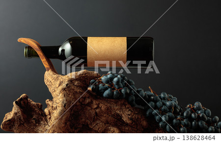 Unopened bottle of red wine, blue grapes, and old weathered snag. 138628464