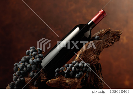 Unopened bottle of red wine, blue grapes, and weathered snag. 138628465