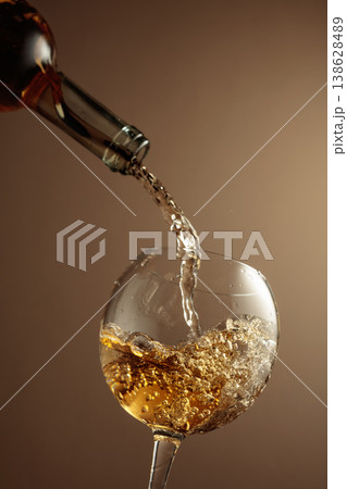 Pouring white wine from a bottle into a glass. 138628489