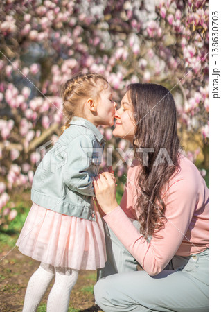 Trendy mom with her little daughter under blooming magnolia trees in a Prague park. Capturing a stylish family moment with a modern approach to parenting 138630703