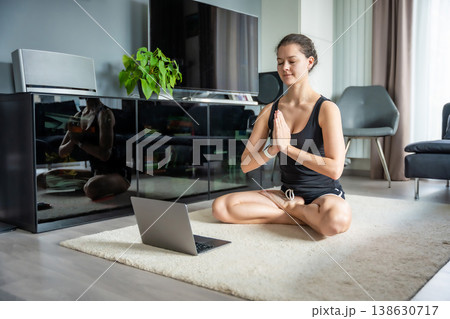 Young woman in sportswear doing yoga exercises on mat in living room. Online workout, fitness, practicing and meditation at home Young woman in sportswear doing yoga exercises on mat in living room. Online workout, fitness, practicing and meditation at home 138630717
