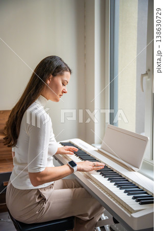 Young woman playing on white piano synthesizer at home. Concept of home lesson of music: learning music enhances motor skills, hearing, and intelligence, fostering creativity 138630729