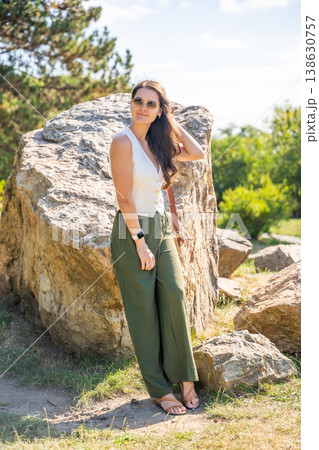 Young woman dressed in white vest and green trousers posing outdoors in Old Money style. Concept of timeless elegance, fashion confidence and classic aesthetic in modern lifestyle. 138630757
