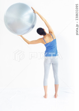 Woman, exercise or ball with back for yoga, exercise or workout on muscle, posture and healthy body. Person, arm or stretching for pilates, training or fitness with sportswear and technique in studio 138631095