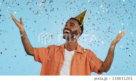 Man, birthday party hat and confetti in studio, smile or surprise for celebration by blue background. Person, event and excited with silver glitter, achievement or happy for winning with wow for goal 138631201