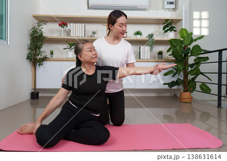 Trainer assisting senior woman in yoga stretch on mat 138631614