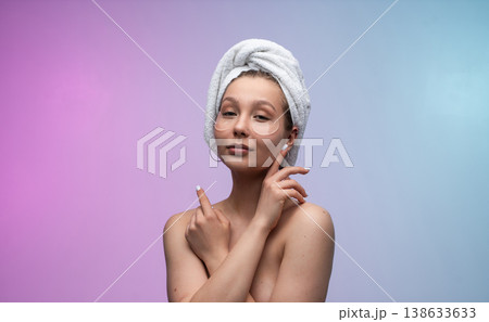 Young woman with a towel turban and hydrating eye patches on her face, embracing a skincare routine for beauty and wellness against a vibrant background 138633633