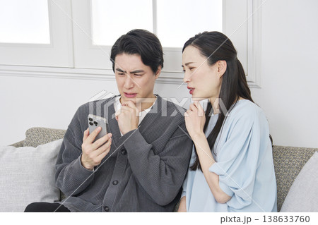 リビングでスマホを見て悩むカップル リビングでスマホを見て悩むカップル 138633760