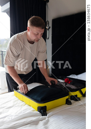 Man packing yellow suitcase on bed preparing for travel Man packing yellow suitcase on bed preparing for travel 138634675
