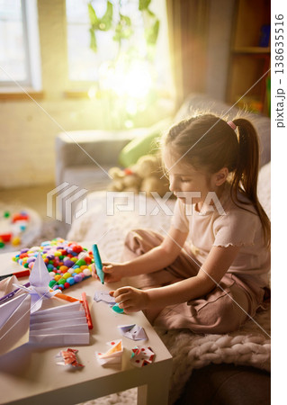 Little girl sitting on sofa making paper crafts and drawing at home 138635516