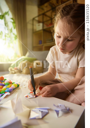 Little girl drawing on paper and decorating paper crafts at table with markers. Little girl drawing on paper and decorating paper crafts at table with markers. 138635520