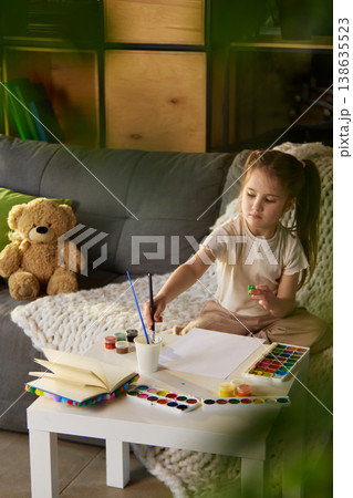 Young girl sitting at table with watercolor paints and blank paper at home. 138635523