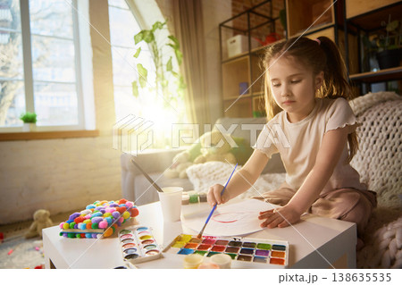 Little girl painting with watercolor set at table in bright cozy living room. Little girl painting with watercolor set at table in bright cozy living room. 138635535