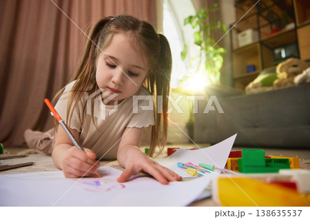 Little girl drawing on paper with warm sunlight flare in modern home interior. 138635537