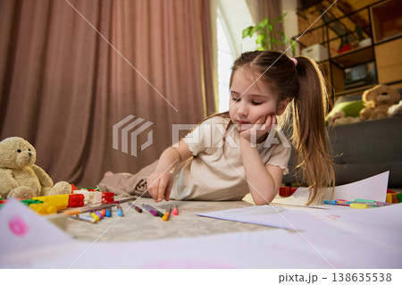 Young girl choosing colored pencils and drawing on paper in cozy living room. 138635538