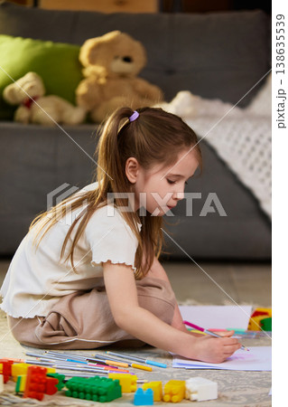 Little girl drawing with colored pencils sitting on floor near toys at home. Little girl drawing with colored pencils sitting on floor near toys at home. 138635539