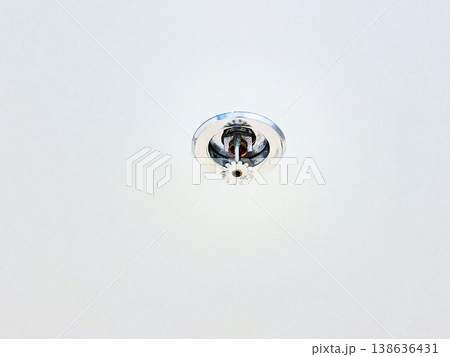 Automatic fire sprinkler head installed on a white ceiling for building safety. High quality photography showing fire protection system, emergency prevention, and indoor security technology 138636431