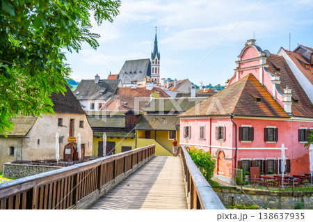 People walk on a wooden bridge in Cesky Krumlov. The town has colorful buildings and a river nearby. Summer skies add brightness to the scene in this UNESCO site. People walk on a wooden bridge in Cesky Krumlov. The town has colorful buildings and a river nearby. Summer skies add brightness to the scene in this UNESCO site. 138637935