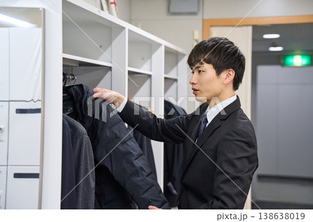 オフィスのロッカーでコートを掛ける若いビジネスマン 出社・退社の風景 オフィスのロッカーでコートを掛ける若いビジネスマン 出社・退社の風景 138638019