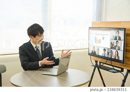 オフィスで大型モニターを使ってオンラインミーティングでプレゼンをする若いビジネスマン オフィスで大型モニターを使ってオンラインミーティングでプレゼンをする若いビジネスマン 138639351
